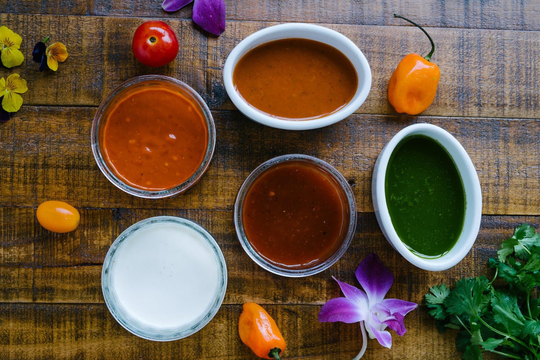 Bowls of red, orange, green and white sauces photographed from above