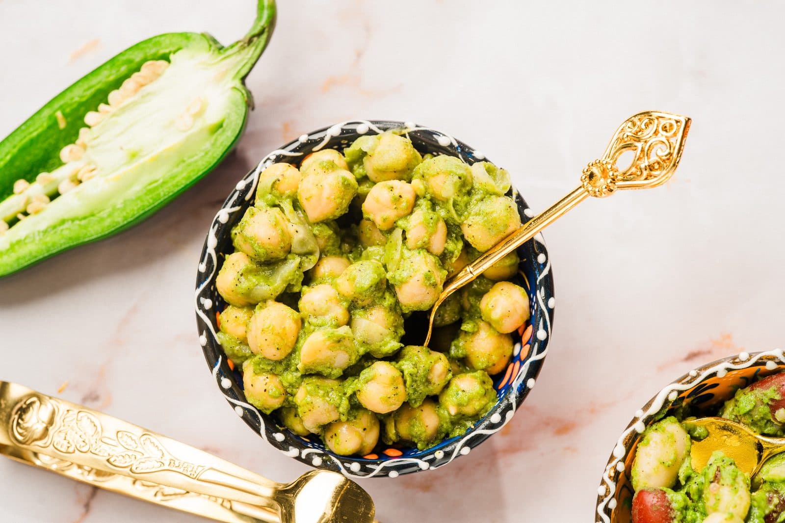 A bowl of chickpeas with herbs, next to a halved green jalapeño