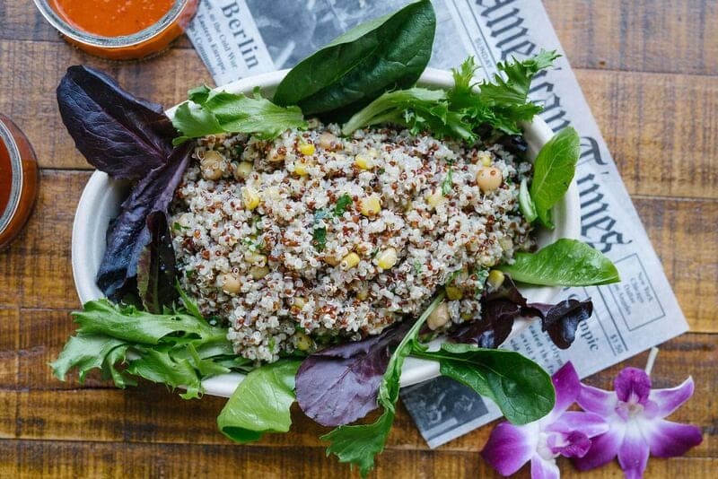 A mound of grains on a bed of mixed leaves with herbs and a purple orchid