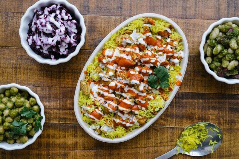 An oval dish of rice with sauce drizzled across it, surrounded by small bowls of sides