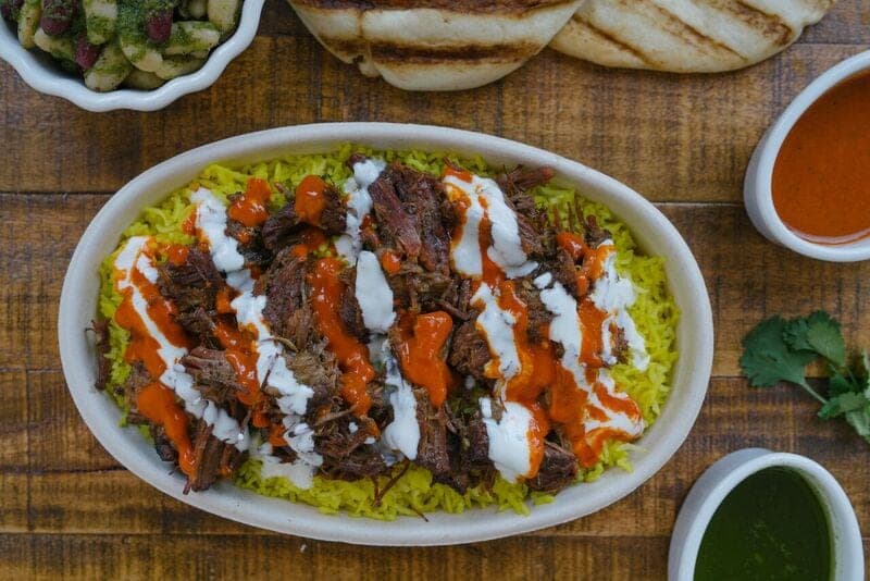 Slow cooked meat over yellow rice with sauces served alongside