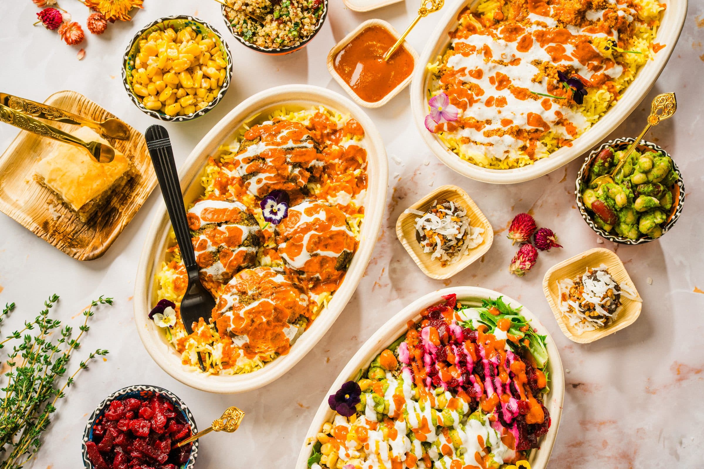 A marble table laid with oval dishes of food, small bowls of sides, sauces and pastry, photographed from above