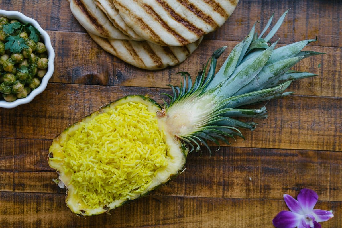 Half a pineapple hollowed out and filled with yellow rice, on a wooden table