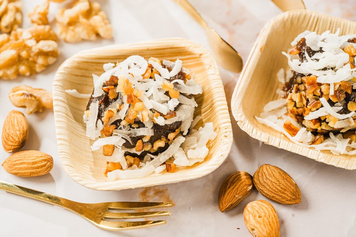 Layered pastry with coconut and nuts in palm leaf dishes, with gold forks on marble