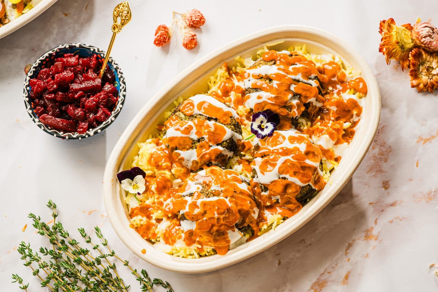 An oval dish of rice finished with orange and white sauce, with a bowl of sides beside it